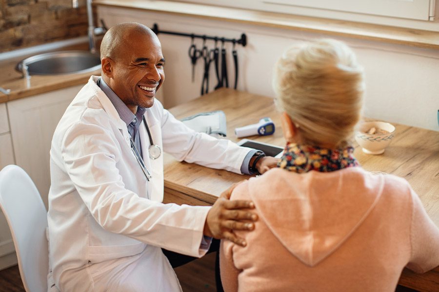 Medicare Advantage Plans - Smiling Doctor Talking to a Woman Patient While Visiting Her at Home