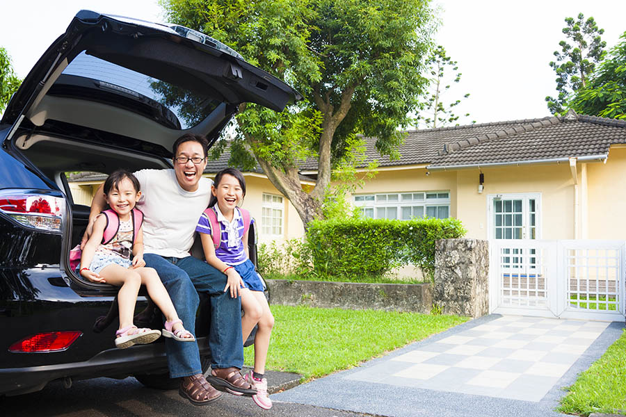 Personal Insurance - Happy Father and Two Small Daughters are Sitting in the Back of Their Car With Their House Behind Them